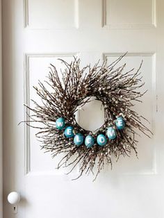 a twig wreath is hung on the front door with blue balls and branches around it