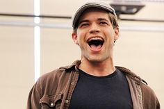 a man laughing while holding a cell phone in his hand and wearing a hat on top of his head