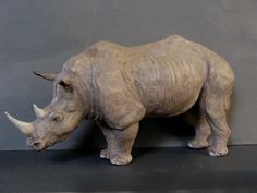 a statue of a rhino standing on top of a black table next to a gray wall