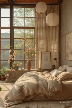 an unmade bed in front of large windows with flowers on the floor and hanging lanterns