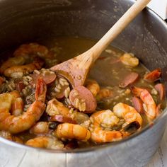 a pot filled with shrimp and sausage next to a wooden spoon on top of a table