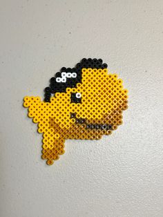 a yellow and black beaded brooch sitting on top of a white wall