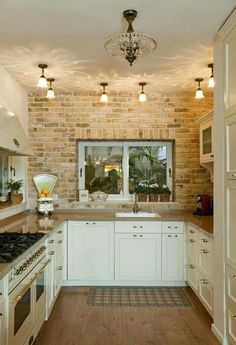 a kitchen with white cabinets and wood flooring next to a brick wall that has an open window