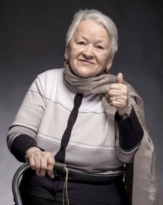 an older woman sitting in a chair with a scarf around her neck giving the thumbs up