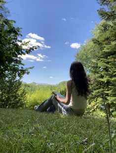 a woman is sitting in the grass and looking up into the sky with her legs crossed