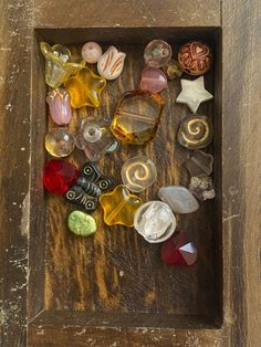 a wooden box filled with lots of different types of glass beads on top of a table