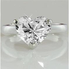 a heart - shaped diamond ring is shown on a white surface, with the reflection of it