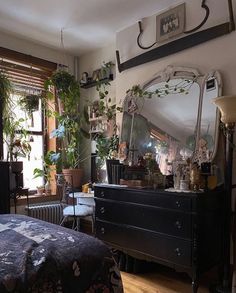 a bedroom with a dresser, mirror and plants on the window sill in it