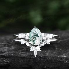 a green and white diamond ring sitting on top of a piece of wood with leaves around it