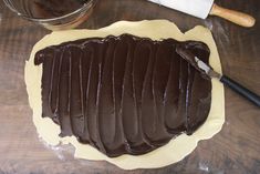 a chocolate cake sitting on top of a wooden table next to a knife and bowl