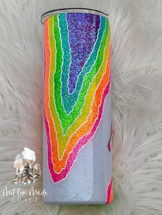 a can that has been painted with rainbows on it and is sitting on a furry surface