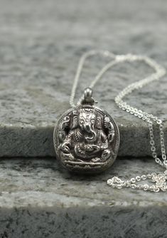 a small silver pendant with an elephant on it's face sitting on a rock