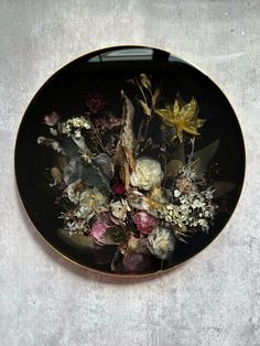 a black plate with flowers on it sitting on a table next to a white wall