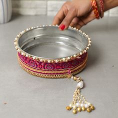 a woman's hand reaching into a metal bowl with beads and tassels