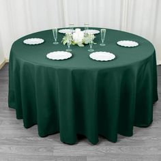 a green table cloth with white plates and flowers on it is set up in front of a window