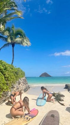 three women in bikinis sitting on the beach with their surfboards next to them