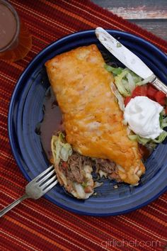 a blue plate topped with food next to a fork and cup on a red table cloth