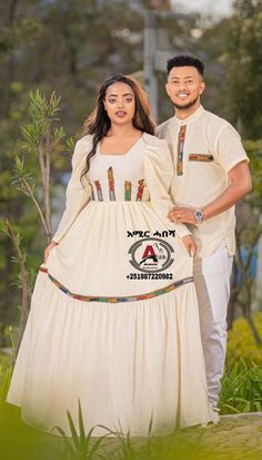 a man and woman standing next to each other in front of some trees wearing traditional african clothing