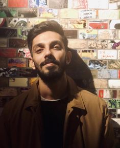 a man with a beard standing in front of a wall full of stickers on it