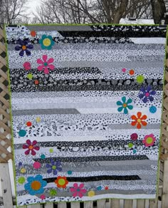 a quilt hanging on a fence in the snow with flowers and stripes all over it