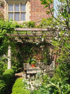 an outdoor dining table surrounded by greenery in front of a brick building with windows