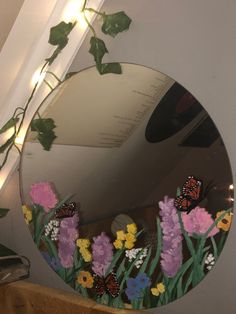 a mirror with flowers and butterflies on it in front of a wall mounted planter