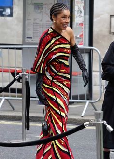 a woman in a red and yellow dress is walking down the street with black gloves on