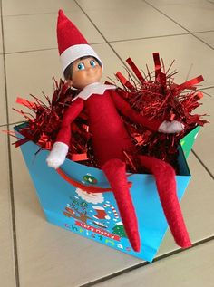 an elf is sitting in a blue box with tinsel on it's legs