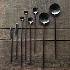 spoons and spatulas lined up on a wooden table, all in different shapes and sizes