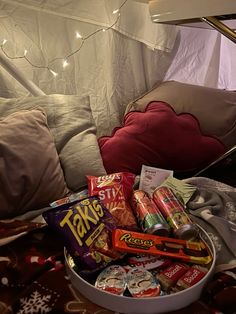 a bucket filled with candy and snacks sitting on top of a bed next to a pillow