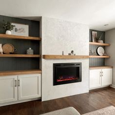 a living room with white cabinets and a fire place in the center, along with open shelving