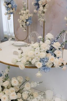 white and blue flowers are arranged on a table in front of two mirrored wall mirrors