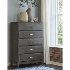 a gray chest of drawers sitting next to a window with a vase on top of it