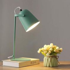 a green lamp sitting on top of a wooden table next to a vase with flowers