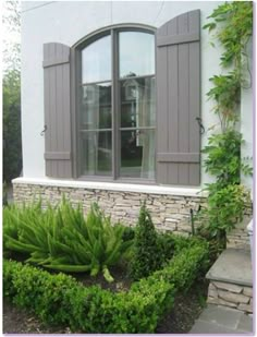 a white house with grey shutters and green plants