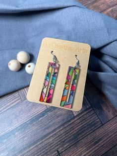 pair of multicolored earrings on wooden table next to blue shirt and white beads