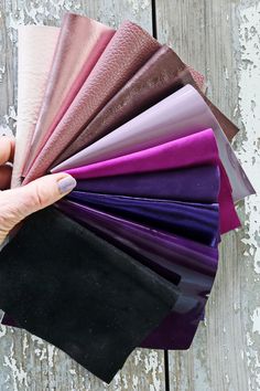 a person holding up some different colors of fabric on a wooden table with white paint