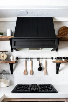 a black stove top oven sitting inside of a kitchen next to wooden shelves with utensils on it