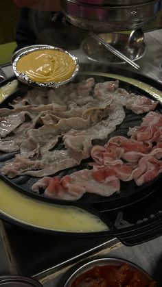 an assortment of meats and sauces on a grill with tongs in the foreground