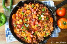 a skillet filled with food sitting on top of a wooden table next to green peppers