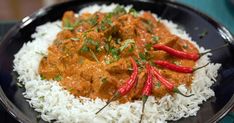 a black plate topped with white rice and meat covered in sauce, garnished with red peppers