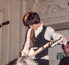 a young man playing an electric guitar while standing in front of a microphone on stage