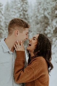 a man and woman laughing together in the snow with trees in the backgroud