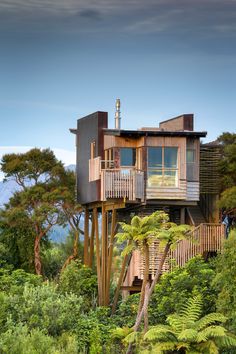 a tree house on top of a hill surrounded by lush green trees and bushes, overlooking the ocean