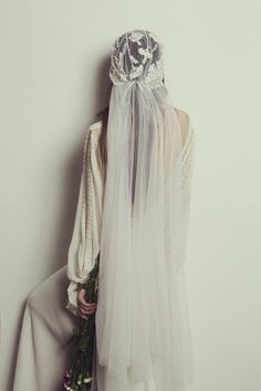 a woman with a veil and flowers in her hair is standing next to a wall