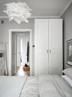 a white bed sitting under a light fixture in a bedroom next to a closet and door