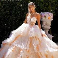 a woman in a white and orange wedding dress standing next to a planter with flowers on it