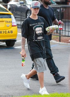 two men walking down the street with drinks in their hands and one holding a can