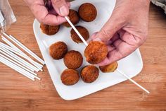 two hands holding chopsticks over some food on a white plate with toothpicks