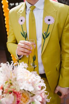 a man in a yellow suit holding a wine glass with flowers on the jacket and tie